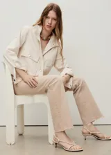 Pantalón de jean color beige claro, tiro medio, estilo campana (flare) con bajo deshilachado y cinco bolsillos.