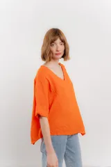 Blusa color naranja confeccionada en 100% lino, con escote en V, mangas cortas con vuelta y silueta amplia. Presenta terminación asimétrica y fila de botones decorativos en uno de los hombros.