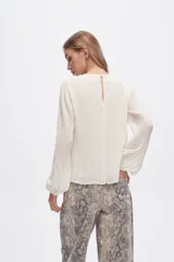 Blusa color verde oliva de poliéster con textura plisada, corte holgado, cuello redondo y mangas largas con puños elásticos.