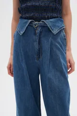 Pantalón jean de tiro alto color azul, con pinzas en la cintura, corte ancho y cierre frontal con botón y cremallera.
