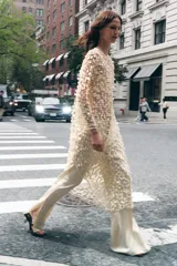 Vestido largo color crema con lentejuelas, de cuello redondo y manga larga. Tiene aberturas laterales en el bajo y cierre con abertura y botón en la espalda.