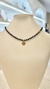 Collar corto de cuentas facetadas color azul oscuro, con dije dorado de trébol de cuatro hojas.