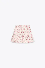 Falda mini con estampado de cerezas rojas sobre fondo blanco, de corte evasé con tablas y cierre lateral oculto.