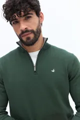Sweater de tejido liso color verde oscuro, con cuello medio y cierre frontal parcial plateado. Presenta puños y cintura acanalados, y un pequeño logo bordado en el pecho.