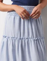 Falda midi a rayas verticales celestes y blancas, con pretina ancha elastizada en punto smock y volados en los cortes.