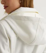 Campera alargada color blanco, confeccionada en polivelour, con cuello alto doblable, mangas largas, abotonado frontal doble, bolsillos y cinturón.