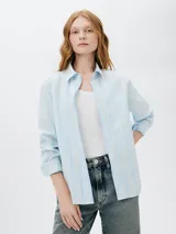 Camisa celeste con rayas verticales blancas, de manga larga y corte clásico.