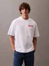 Remera blanca de algodón con cuello redondo, mangas cortas y logo de Calvin Klein Jeans estampado verticalmente en color rojo en el pecho.