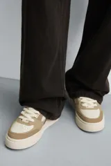 Zapatillas deportivas de estilo retro, color beige y marrón, con cordones y suela gruesa.