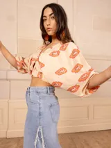 Top corto color crema con estampado de cachemir en tonos naranja y rosa, escote elástico con volantes, mangas cortas abullonadas y corte crop.