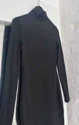 Vestido corto negro de mangas largas y cuello alto.