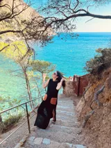 Vestido largo tejido de algodón color negro, sin mangas, con cuello redondo y tajos laterales. Presenta dos bolsillos de cuero color marrón en el frente.