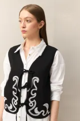 Chaleco blanco de algodón con bordados de cadenas doradas y lazos frontales.