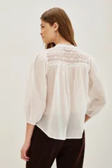 Camisa de algodón color celeste, con escote en V, cierre parcial de botones y detalles de encaje en los hombros. Mangas largas abullonadas con puños elásticos.