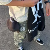 Camiseta negra con efecto acid wash, corte oversize y estampado trasero blanco con el texto "lm" sobre una estrella y el texto "lookmom" debajo.