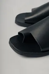Sandalias planas de cuero color negro, con tira ancha sobre el empeine y diseño minimalista.