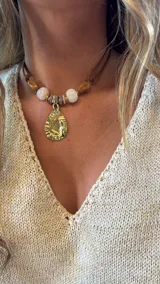 Gargantilla con cuentas de piedra blanca y marrón, con dije dorado en forma de lágrima.