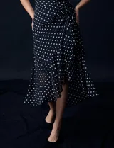Vestido midi de gasa color negro con lunares blancos, con mangas cortas, escote redondo y ruedo asimétrico. Presenta un frunce lateral con lazo de ajuste.