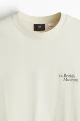 Remera color crema de corte holgado con cuello redondo y estampado pequeño con el texto "The British Museum" en el pecho.