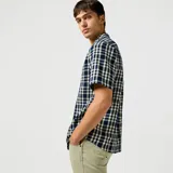 Camisa de manga corta a cuadros azules y blancos, con cuello clásico y bolsillo en el pecho.