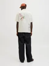 Camisa de manga corta color crema con estampado de flores y hojas en tonos naranja y verde. Tiene cuello resort, cierre frontal con botones y calce relajado.