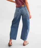 Jean de denim azul claro con lavado desgastado, tiro medio y pierna ancha. Presenta roturas y paneles con costuras visibles en la parte delantera de las piernas.