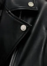 Campera de cuero ovino negra, estilo biker, con cuello con solapa, cierre frontal asimétrico con cremallera, mangas largas con cremallera en los puños y dos bolsillos laterales con cremallera. Tiene forro interior.