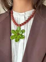 Collar corto con cuentas color ladrillo y dije de flor verde con centro marrón.