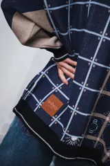 Cardigan oversized de tejido jacquard color crema con diseño de cuadrados en marrón y detalles bordados. Tiene cuello en V, cierre con botones, mangas largas y bolsillos frontales.