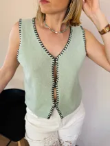 Chaleco tejido color arena con terminaciones en punto festón negro.