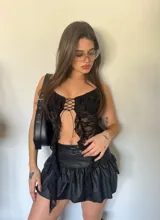Top de encaje negro con volados, lazo cruzado en el pecho y corte asimétrico.