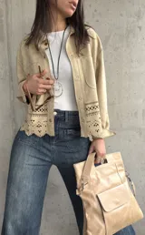 Sobrecamisa beige de gamuza con cuello camisero, cierre frontal con botones y mangas largas con puños abotonados. Presenta bolsillos de parche en el pecho y detalle de calado en el ruedo.