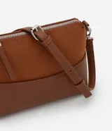 Cartera de hombro pequeña marca Satinato, color marrón, con diseño dividido en dos texturas: parte superior aterciopelada (suede sintético) y parte inferior lisa de cuero sintético. Cuenta con bolsillo delantero amplio, asa ajustable y desmontable con herrajes metálicos plateados, y cierre superior con cremallera y tirador alargado.