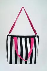 Bolso tipo tote bag con diseño a rayas verticales blancas y negras, doble asa de mano rosa y correa de hombro ajustable y removible también rosa.