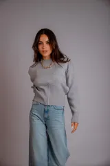 Buzo gris de punto con cuello redondo, mangas largas abullonadas y cierre frontal asimétrico.