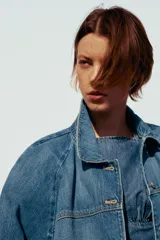 Cazadora de denim azul de corte holgado, con cuello solapa y manga tres cuartos acabada en puño. Cierre frontal con botones metálicos.