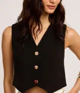 Chaleco negro de crepé con escote en V y abotonadura dorada. Corte slim y sin mangas.