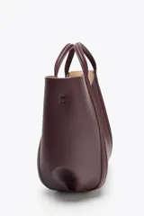 Bolso mini city color borgoña, con asa de mano y asa bandolera extraíble. Tiene detalle de pespuntes en contraste y bolsa interior extraíble con cierre de cremallera.