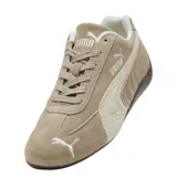 Zapatilla Puma de perfil bajo, estilo automovilismo, color beige/marrón claro con detalles en blanco. Presenta una capellada de gamuza, la icónica franja Puma en un tono más claro y suela de goma marrón oscuro.