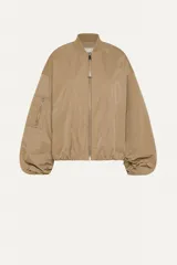 Campera bomber color beige, corte regular, con cierre frontal con cremallera visible, cuello acanalado, puños y bajo elásticos fruncidos, hombro caído, bolsillos de ribete verticales y bolsillo utilitario con cremallera en la manga.