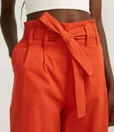 Pantalón clochard color naranja, con cintura elástica, cinturón para atar, cierre por cremallera, pliegues delanteros y barra doblada.