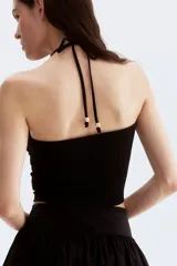 Top corto negro de punto con textura, corte entallado, escote halter y tiras finas con cuentas en los extremos.