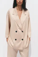 Blazer color beige de cuello solapa y manga tres cuartos. Tejido con efecto arrugado y cierre frontal cruzado con botones negros.
