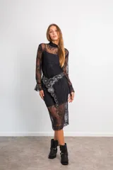 Conjunto de encaje negro, compuesto por una blusa semitransparente de manga larga con cuello alto y una falda midi recta con viso a tono.