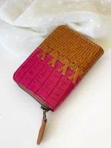 Billetera pequeña de cuero color fucsia y marrón con textura tipo piel de cocodrilo. Tiene cierre metálico y detalle de tiras de cuero cruzadas en el frente.