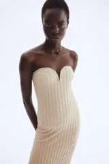 Vestido midi ajustado color beige, sin tirantes (strapless), con escote corazón que incluye un alambre de metal revestido para soporte y un borde de silicona oculto para mejor ajuste. El tejido presenta una textura plisada o arrugada vertical.