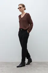 Pantalón negro de vestir, corte recto y tiro alto, con pliegues frontales y puños doblados. Se complementa con un cinturón fino negro con hebilla metálica en forma de símbolo.