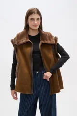 Chaleco marrón de gamuza sintética con cuello y borde de piel sintética. Cierre frontal con cremallera y bolsillos laterales.