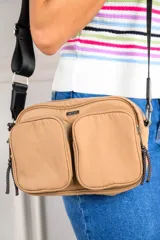 Cartera bandolera color beige con dos bolsillos frontales con cierre y correa ancha negra regulable.