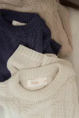 Sweater tejido en hilo de algodón color crudo, con cuello redondo, corte holgado, hombros caídos y diseño de ochos en la parte delantera.